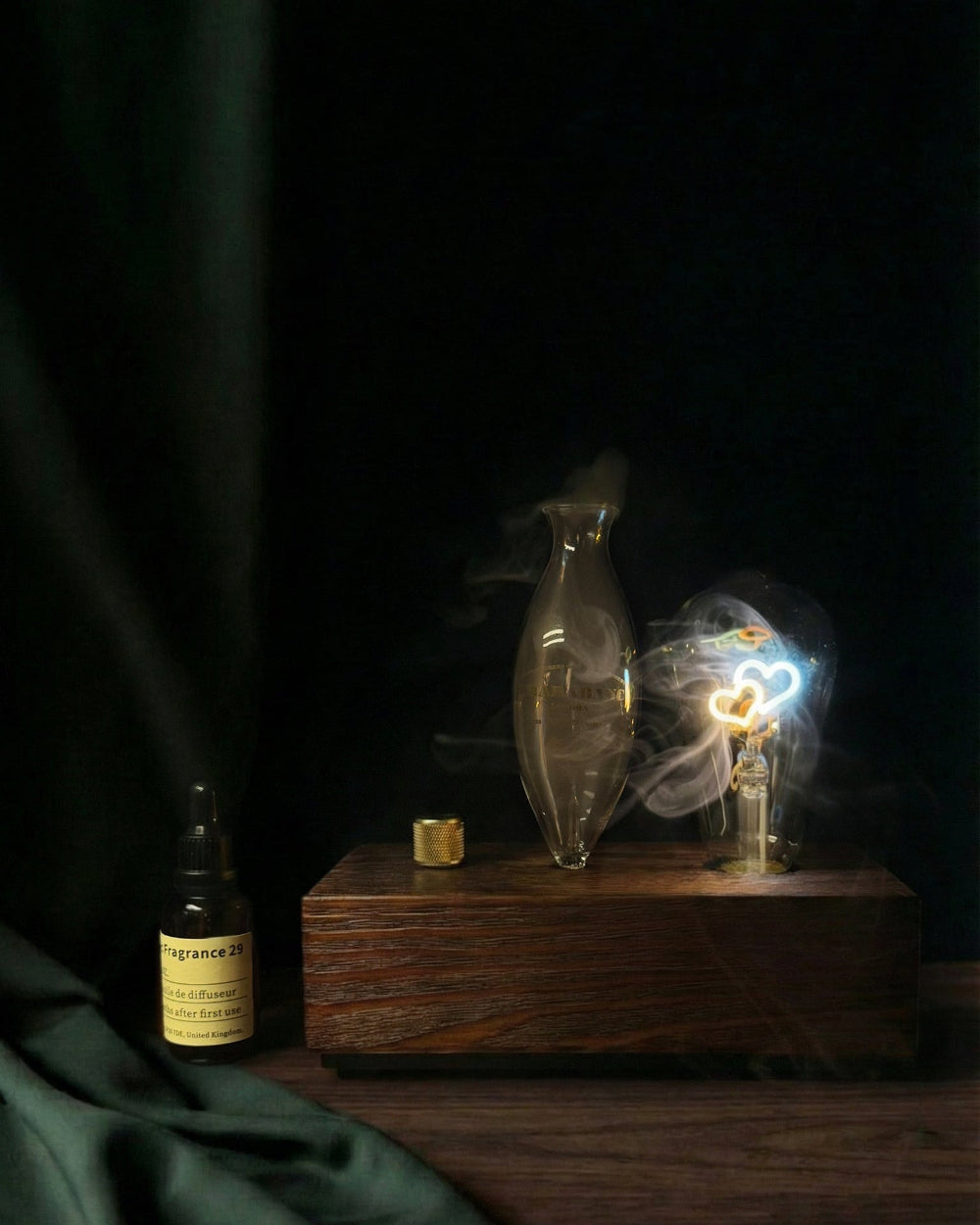 "A warm, detailed close-up of the chavanc-aromawaterless nebulizing diffuser. The delicate hand-blown glass nebulizer is positioned next to a glowing Edison-style filament bulb, both mounted on a solid dark wood base with a knurled metallic dial. A bottle of chavanc-aroma 29 santal essential oil sits beside it, highlighting the artisanal quality."