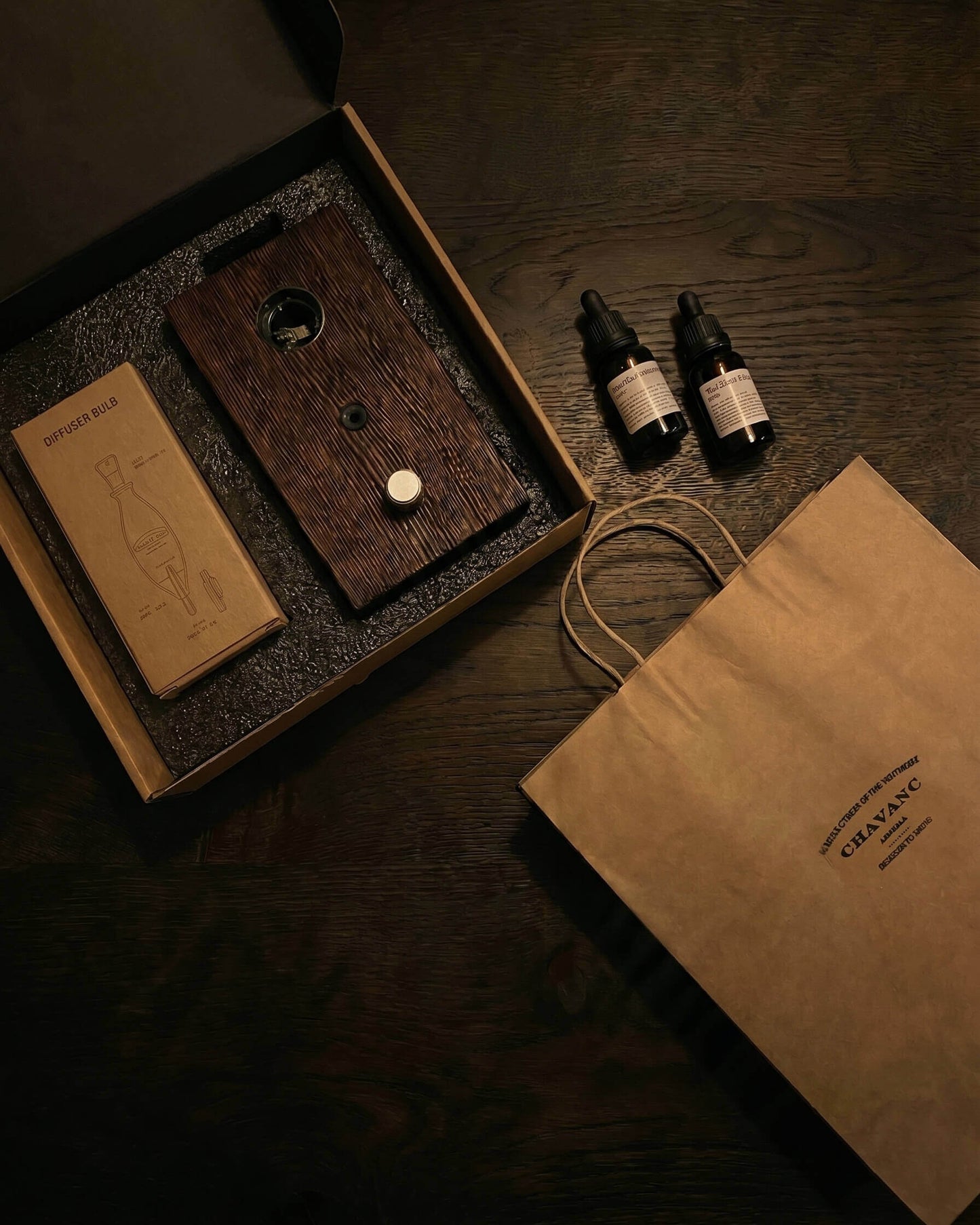 A top-down overhead shot of the chavanc-aromagift set in its open packaging. The dark wood diffuser base, a brown kraft paper box for the nebulizer, and a small essential oil bottle are neatly nestled in a precision-cut black foam insert, reflecting a minimal and sustainable luxury design."