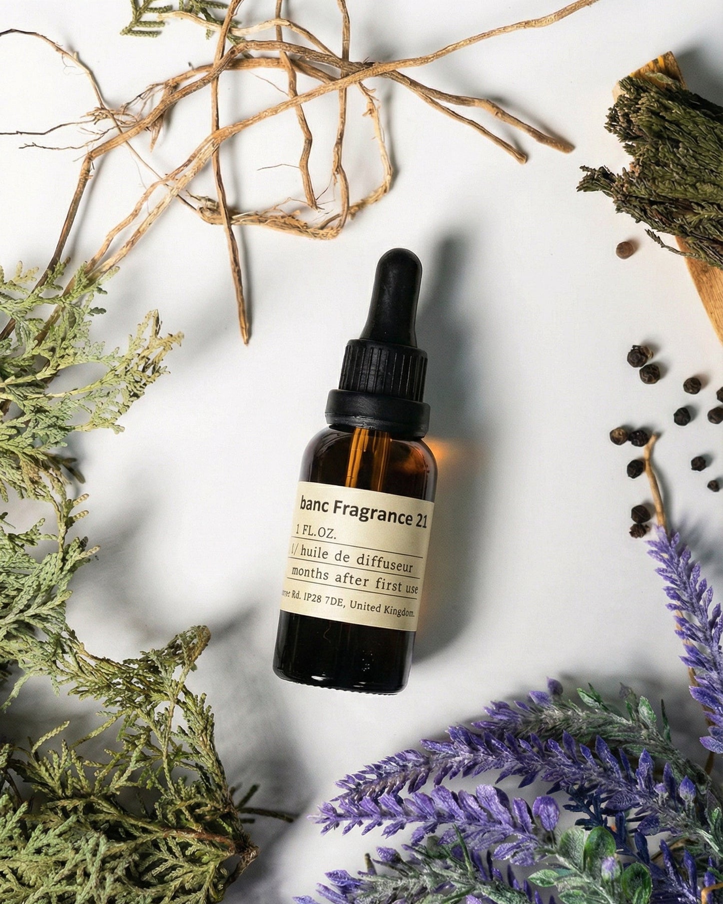 Chavanc AromaNO.21 Wild Horizon essential oil bottle surrounded by purple lavender sprigs, black peppercorns, green cedar branches, and rustic wood sticks on a clean background.