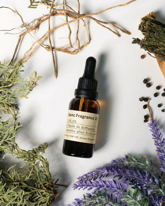 Chavanc AromaNO.21 Wild Horizon essential oil bottle surrounded by purple lavender sprigs, black peppercorns, green cedar branches, and rustic wood sticks on a clean background.