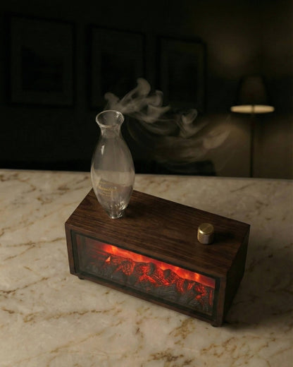 Chavanc Aroma waterless essential oil diffuser, handcrafted walnut wood with a realistic LED fireplace effect, positioned on a sunlit limestone shelf next to a brand-labeled fragrance dropper bottle. Striking geometric shadow on a textured wall."