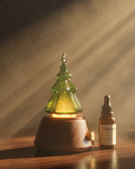 A luxury Chavanc emerald green glass Christmas tree nebulizing diffuser resting on a floating walnut shelf in a master bedroom. The background features a dark green marble-tiled wall, beige textured pillows, and a golden-framed botanical print. The internal iLED light is on, casting a warm amber glow through the green tinted glass.