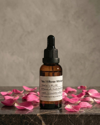 Chavanc aroma  NO.11 Rose Whisper essential oil bottle surrounded by blooming pink roses, dried rosebuds, and earthy botanical accents on a white surface.