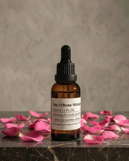 Chavanc aroma  NO.11 Rose Whisper essential oil bottle surrounded by blooming pink roses, dried rosebuds, and earthy botanical accents on a white surface.