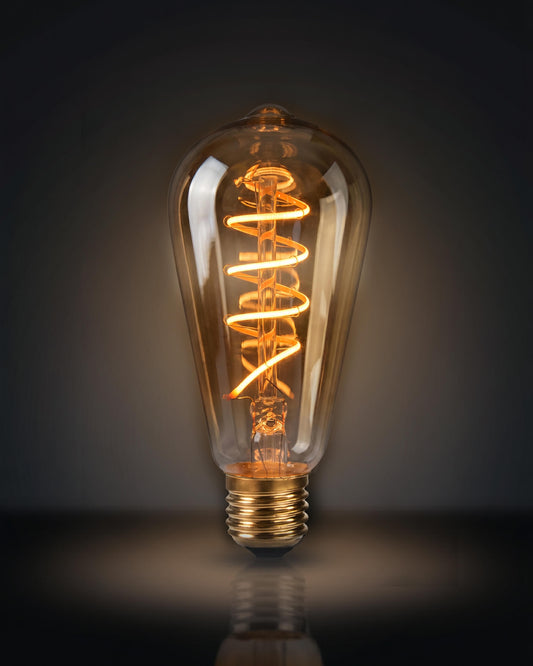 Detailed close-up photograph of a clear glass specialized replacement bulb for a chavanc- aroma aromatherapy diffuser, featuring a unique orange spiral helix-shaped decorative filament. The vintage Edison-style bulb rests on two ornate, stacked cream-colored ceramic plates with scalloped edges and beaded borders. An aesthetic and retro accessory for home fragrance and luxury interior decor.
