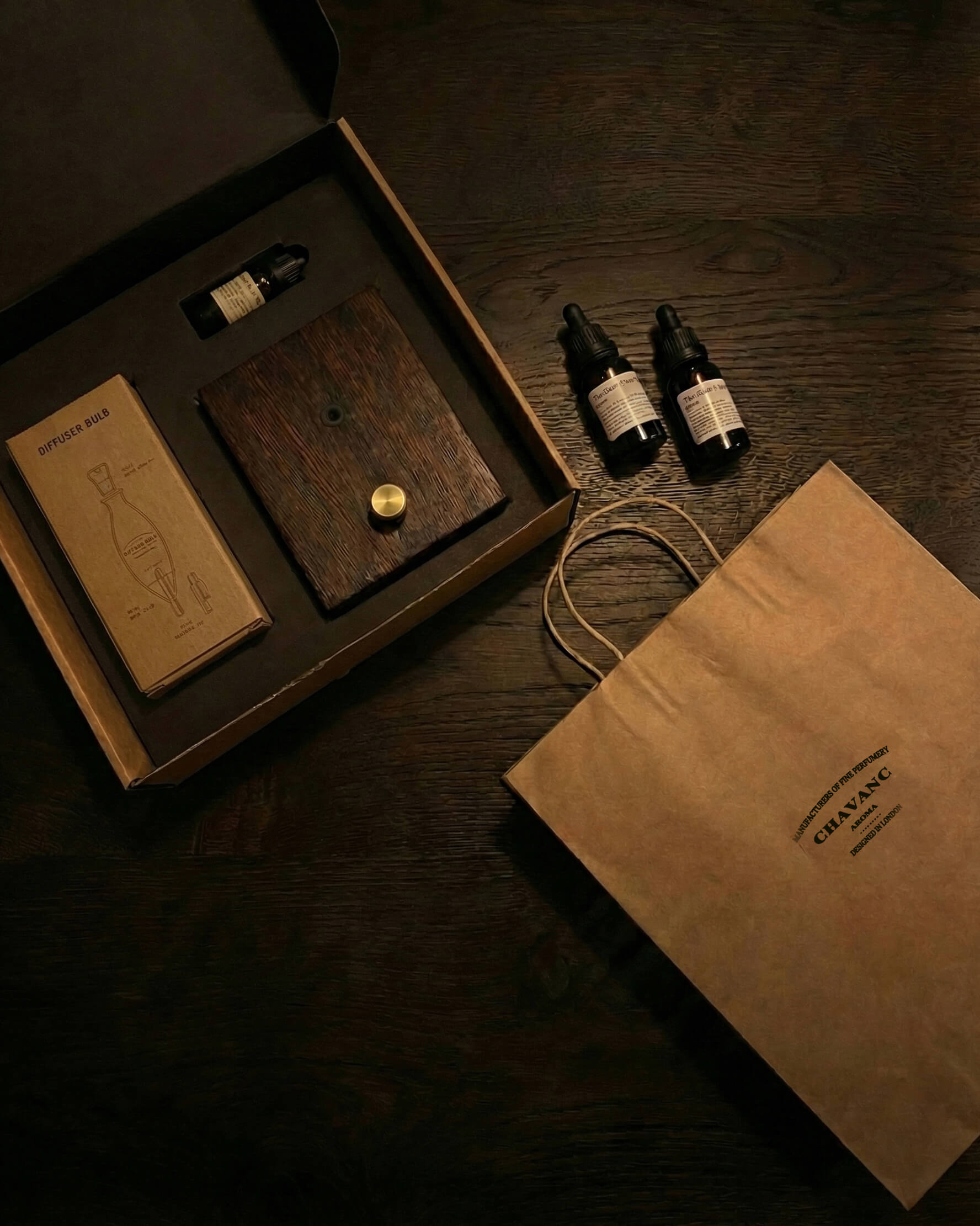 "A top-down overhead shot of the chavanc-aroma gift set in its open packaging. The dark wood diffuser base, a brown kraft paper box for the nebulizer, and a small essential oil bottle are neatly nestled in a precision-cut black foam insert, reflecting a minimal and sustainable luxury design."