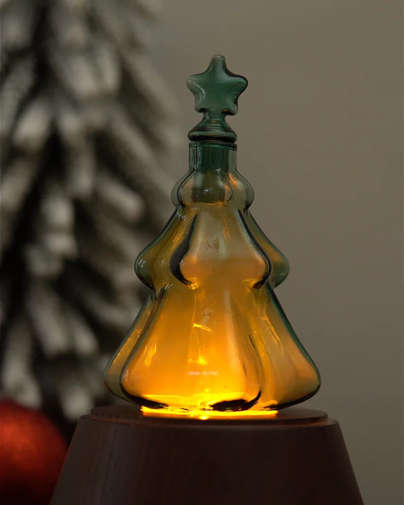 Emerald green Christmas tree glass diffuser reservoir illuminated with warm glowing ambient light on solid wood base