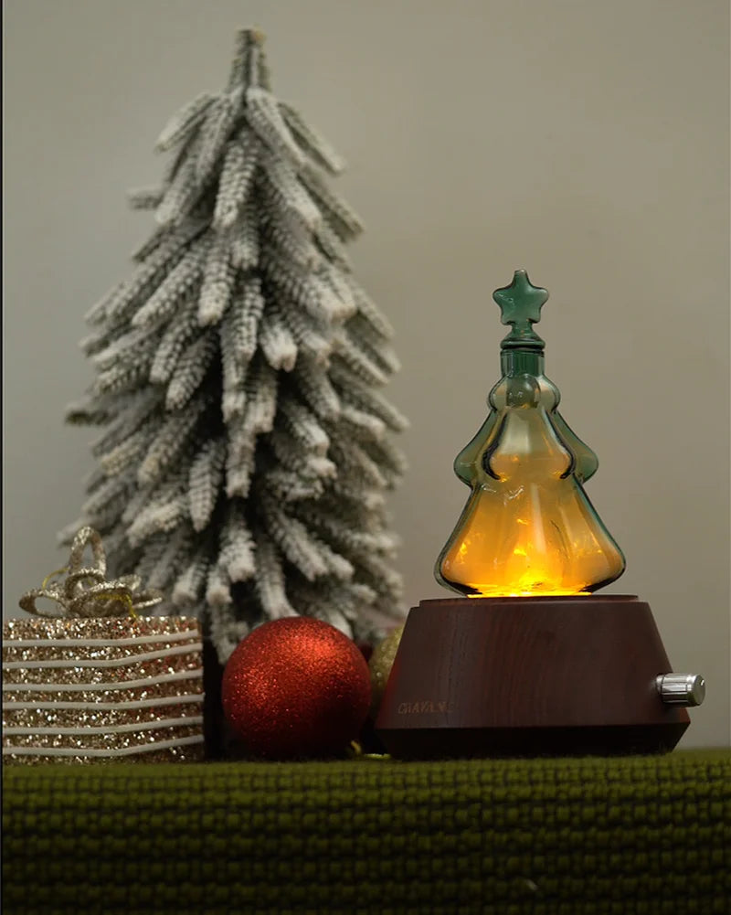 Emerald green Christmas tree nebulizing glass reservoir installed on solid wood aroma diffuser base glowing with warm ambient light